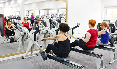 A row of women using rowing machines in front of a mirrored wall, 33Ƶ