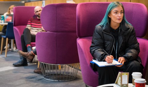 Student with vibrant blue hair sat on purple pod seat in 33Ƶ Atrium